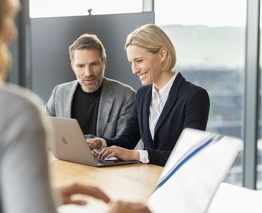 A man and a woman are working together on a laptop and smiling.