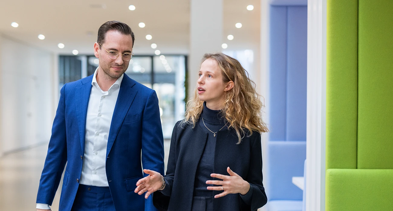 Das Bild zeigt zwei Personen in einer Unternehmensumgebung, die offenbar ein Gespräch oder eine Diskussion führen.